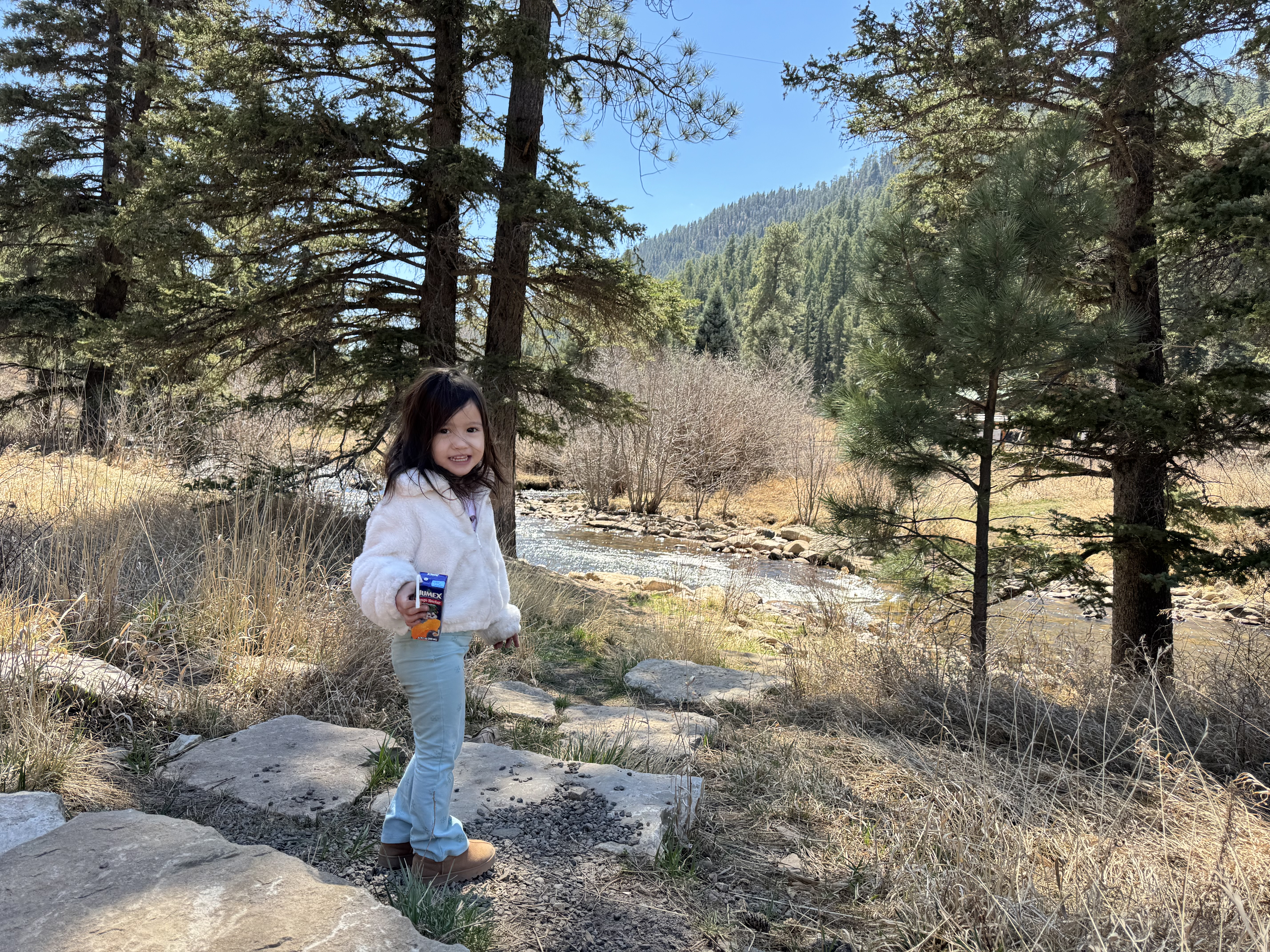 Young child standing by the Pecos River with mountains and pines behind